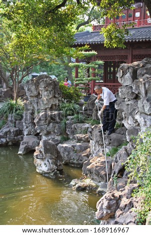 Shanghai, China - July 24, 2007: Gardener cleaning a pond in Yuyuan gardens on July 24, 2007. Yuyuan garden is one of the most beautiful gardens in China.