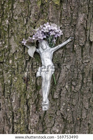 Small Christ figurine decorated with flowers nailed to the tree bark at a roadside shrine.