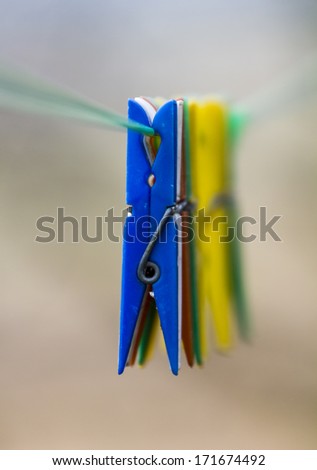 Row of colorful clothespins hanging from  rope;  first blue clothespin in focus, other clothespins and background blurred