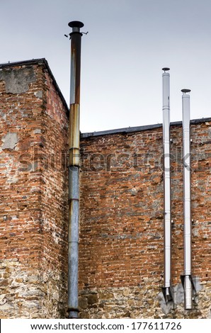 three metal chimneys, one old and rusty and two new and shiny attached to a shabby brick wall of an old building