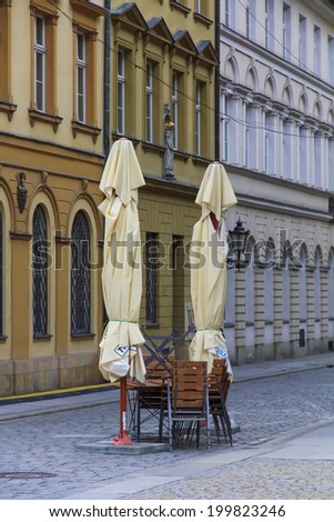 two convoluted restaurant umbrellas, chairs and table with facades of old houses in background