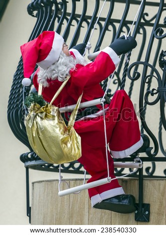 Big figurine of Santa Claus with a  bag on its back, attached to a house\'s balcony so as it appears to be climbing inside