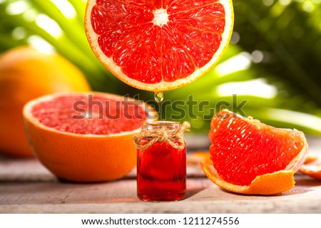 Bottle of essential oil from grapefruits on wooden table and green leaves background - alternative medicine