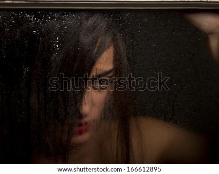 Beautiful girl looks out of the window with raindrops.