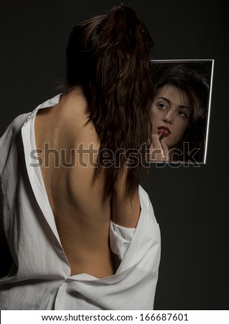 Beautiful woman with man\'s shirt puts her lipstick on looking in the mirror.