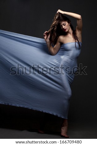 Beautiful young girl dancing with blue fabric on a gray background.