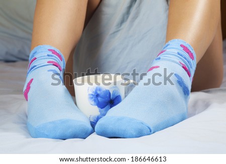 A cup of coffee or hot chocolate and female feet with socks on a blue sheets.