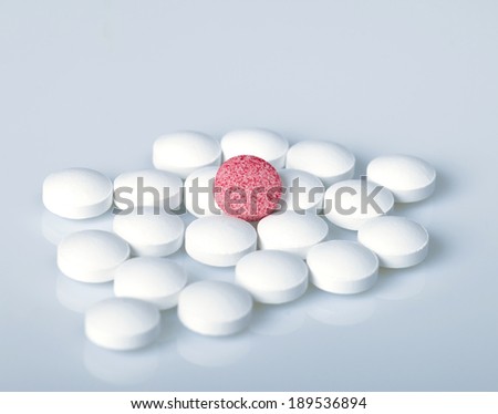 White spilled pills and only one pink pill on a blue background. Macro
