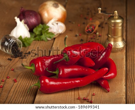 Red Hot Chili Peppers over wooden background. In the background there are a spoon with grains of black, green and red pepper, grinder, onion, garlic and parsley.
