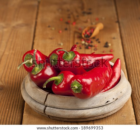 Red Hot Chili Peppers in bowl and spoon with grains of black, green and red pepper over wooden background.