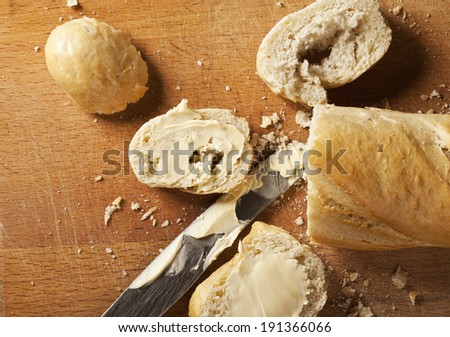French bread baguette and its slices with butter and metal knife on wooden background.