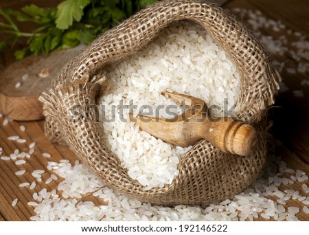 White rice in a sack and wooden scoops on wooden background.
