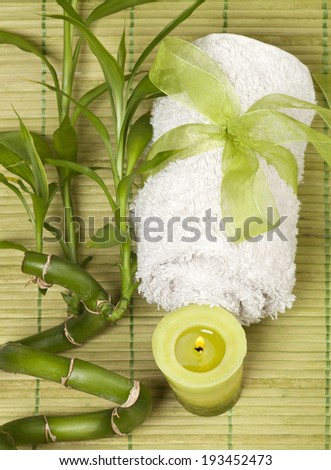 Spa background with rolled towel and green candle with bamboo on green pad.
