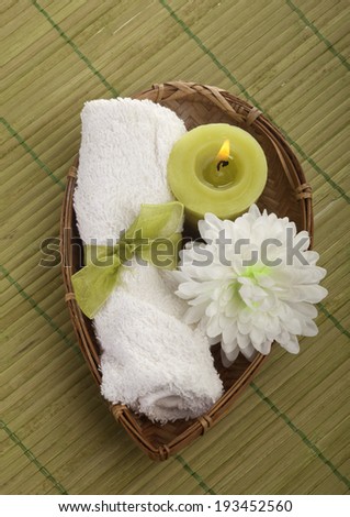 Spa background with rolled towel and green candle with flower in a basket.