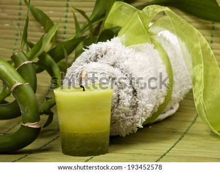Spa background with rolled towel, green candle and bamboo on green pad.