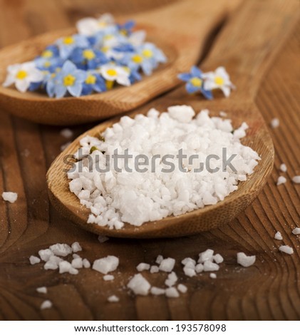 Spa background with sea salt and flowers in wooden spoons on wooden background.