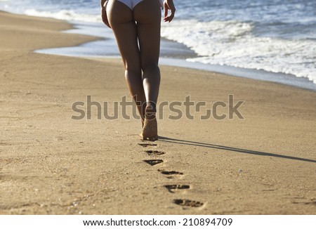 Young woman walking alone on the sand beach in the sunset and leave footprints behind. Focus on the food and the sand.