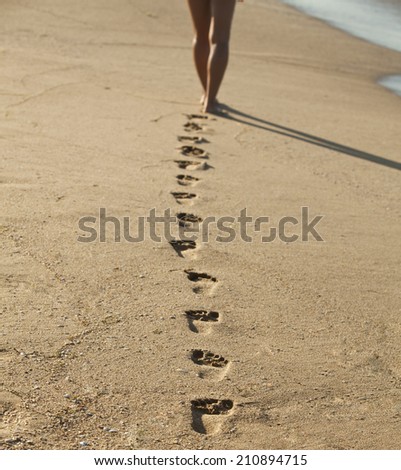 Young woman walking alone on the sand beach in the sunset and leave footprints behind. Focus on the steps in the sand.