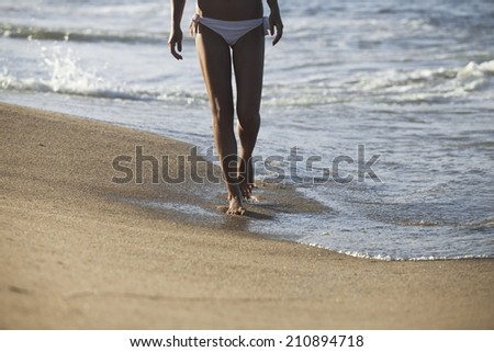 Young woman walking alone on the sand beach in the sunset.