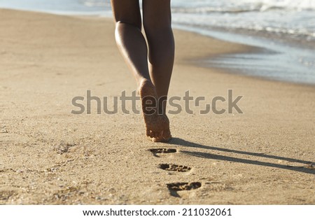 Young woman walking alone on the sand beach in the sunset and leave footprints behind. Focus on the food and the last step in the sand.