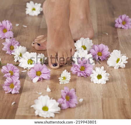 Feminine feet and flowers on a parquet floor.