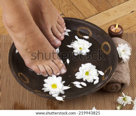 Feminine feet in foot spa bowl with flowers, towel and candle.