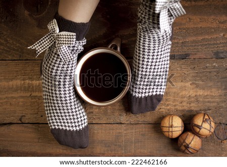 A cup of coffee or hot chocolate and female feet with sweet brown socks on a wooden background.
