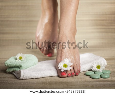 Female feet with drops of water, towel, flowers and spa rocks.