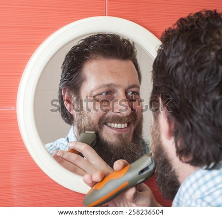 Bearded man trim his beard with electric shaver.