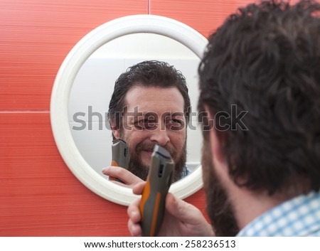 Bearded man trim his beard with electric shaver.