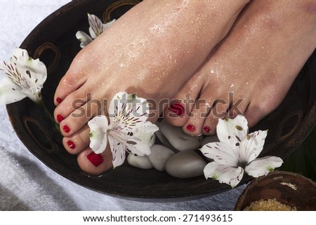 Female feet with drops of water soaked in spa bowl with flowers and rocks.