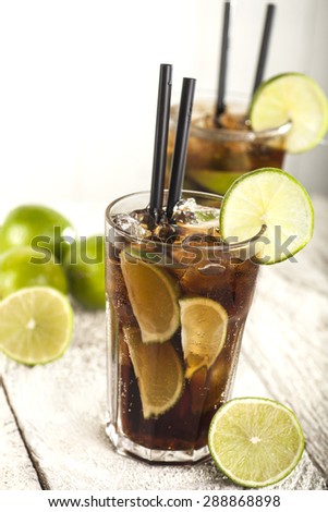 Cuba Libre Cocktail with lime on a white wooden background