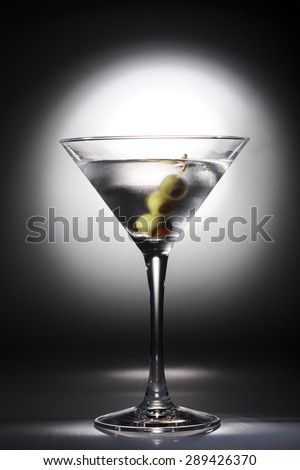 Sweaty glass of martini cocktail with olives on black background with white spot light.
