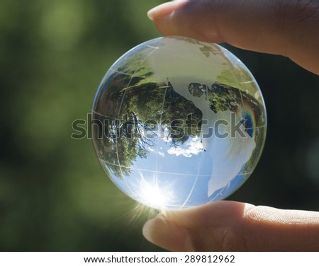 World environmental concept. Crystal globe in human hand on beautiful green and blue bokeh. Visible are the continents the Americas. Selective focus on the reflection.
