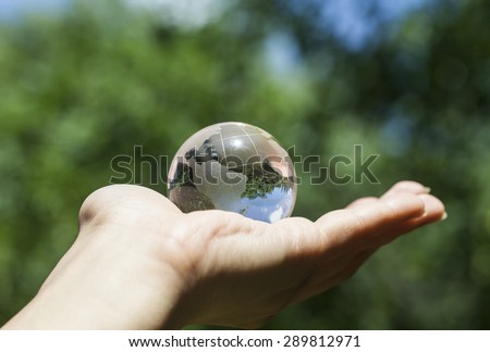 World environmental concept. Crystal globe in human hand on beautiful green and blue bokeh. Visible are the continents the Americas. Selective focus on the reflection.