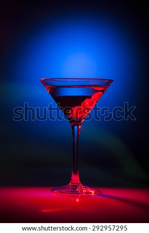 Glass of martini cocktail with red cherries on a mixed color background.