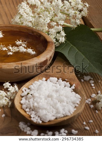 Spa background with sea salt in a spoon and bowl with water and flowers on wooden background.
