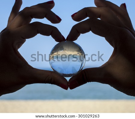 Environmental concept - close up of human hands showing heart shape gesture and holding crystal globe.