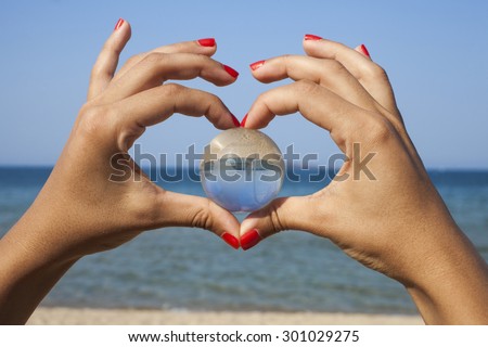 Environmental concept - close up of human hands showing heart shape gesture and holding crystal globe.