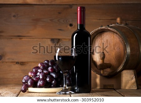 Wine bottle with glass, bunch of grapes and wooden barrel on old wooden background