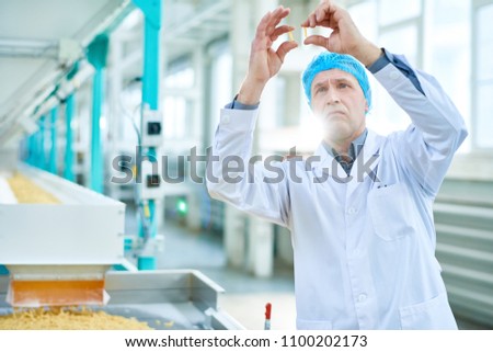 Waist up portrait of senior factory worker doing quality inspection in food industry holding two macaronis standing by conveyor belt, copy space