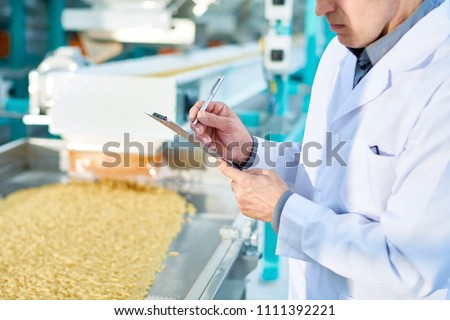 Mid section portrait  of  unrecognizable factory worker doing  production quality inspection in food industry holding clipboard and standing by conveyor belt, copy space