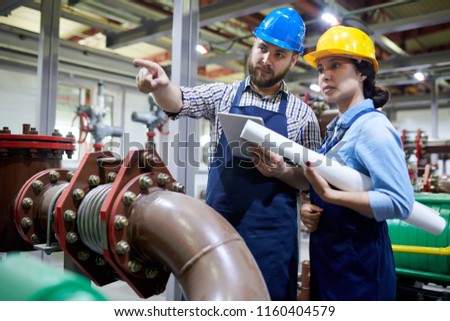 Portrait of two factory workers pointing away while working with piping and machines in modern workshop, copy space