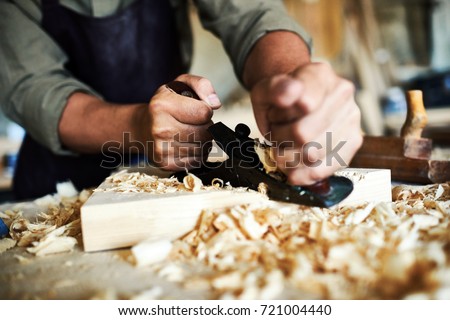 Closeup portrait of strong male hands shaving piece of wood with plane tool in carpenters workshop making furniture