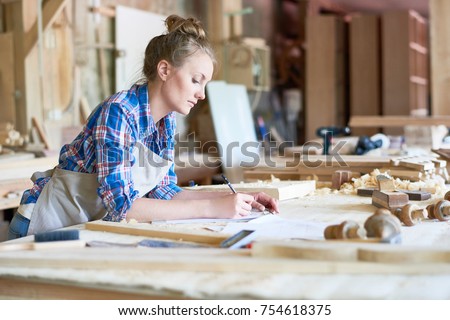 Side view portrait of young woman making notes standing at table in modern workshop, copy space