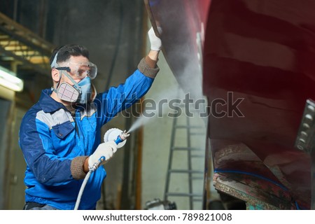 Side view portrait of  worker wearing protective mask spray painting boat in yacht workshop  copy space