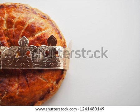 A whole homemade Twelfth Night cake (galette des rois) on white background, crown around the pie, just one half seen on the left side