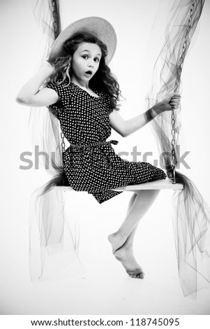 Beautiful retro style portait of nine year old girl in dress and summer hat on swing over white.