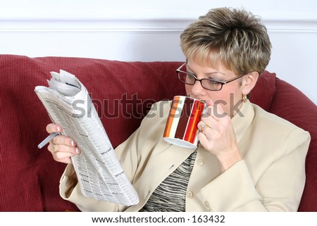 Beautiful woman in business suit on the sofa with coffee and newspaper.