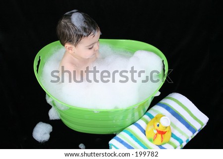 Two year old boy in a green tub of bubble water with bubbles on his head.